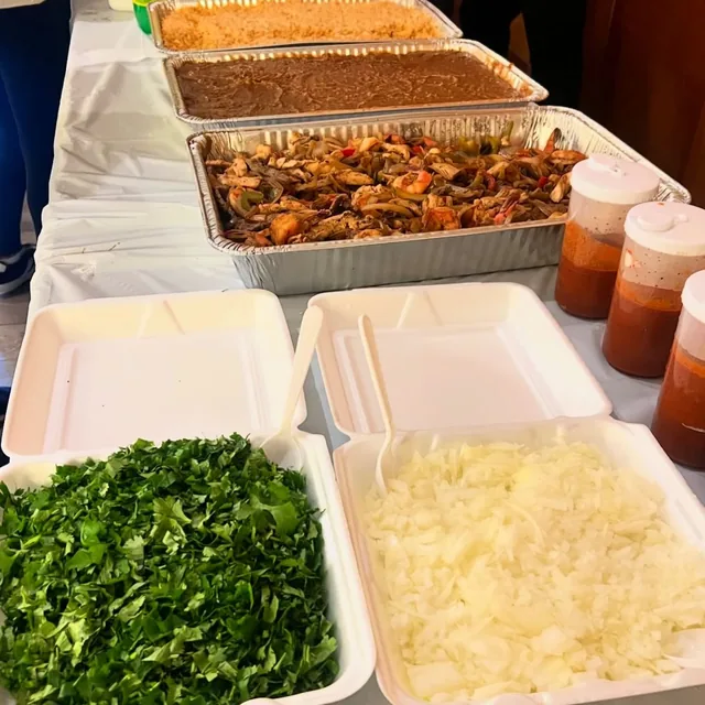 A catering spread of sizzling fajitas, rice, beans and fresh cilantro and onion